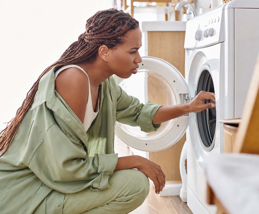 Woman crouches beside an open washer while checking the inside of the machine