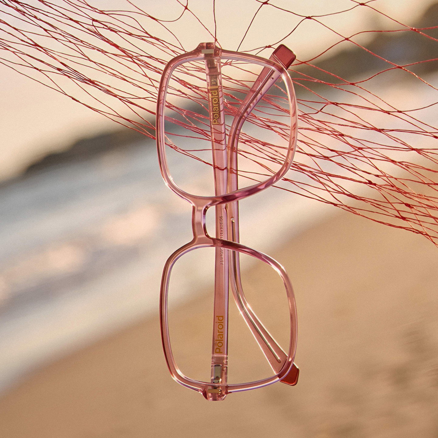 Rosafarbene Brille hängt in einem roten Fischernetz vor Strand und Meer im Hintergrund.
