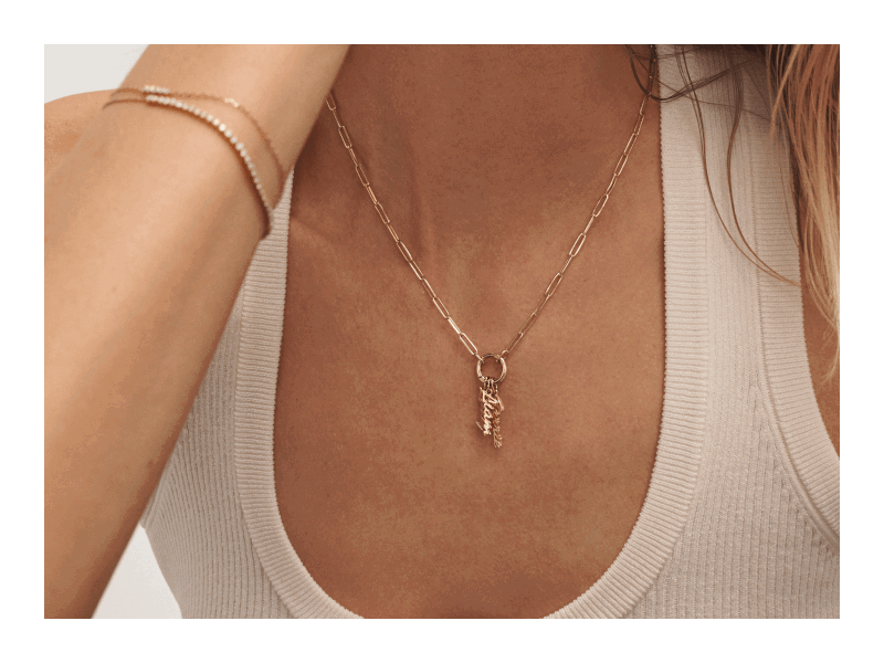 A model wearing a gold paperclip chain necklace with sparkling letter charms, and bracelets.