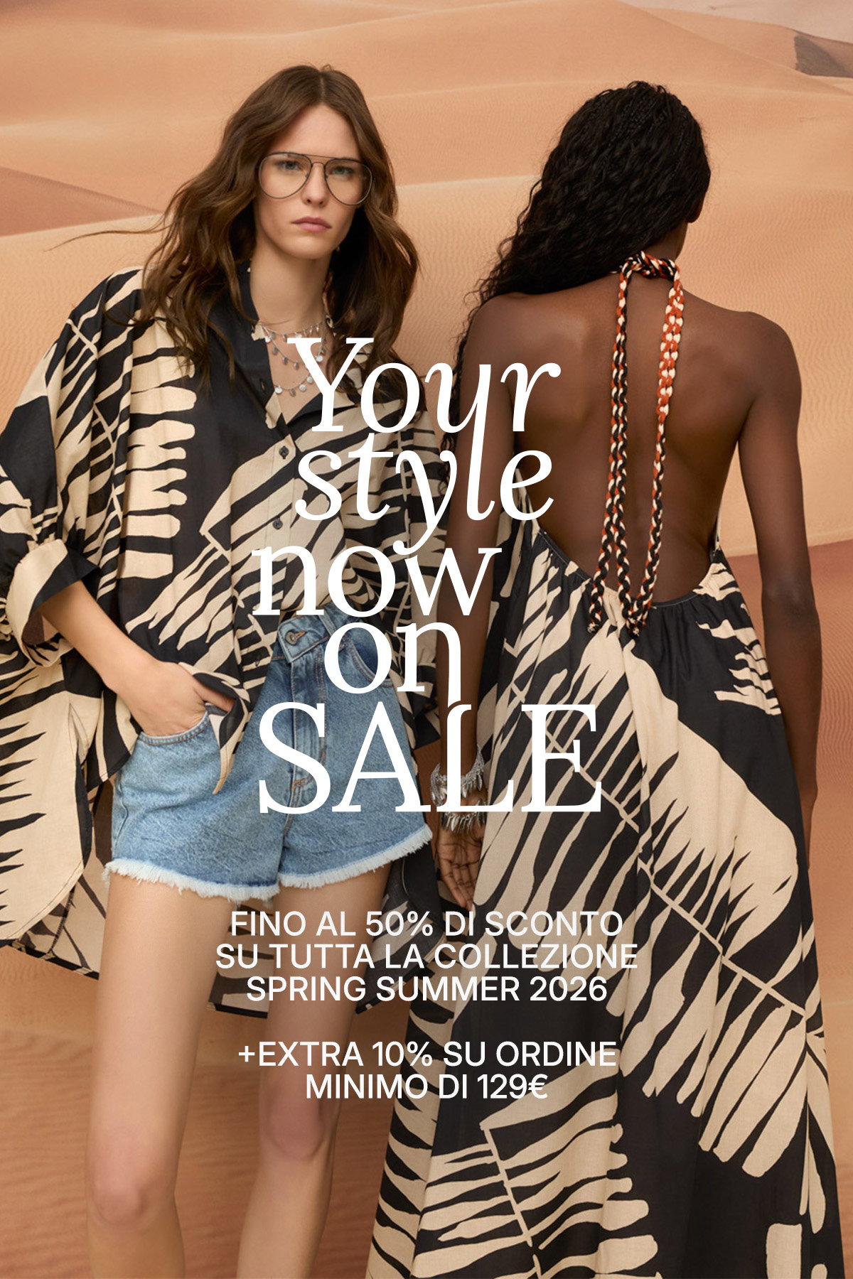 Two women modelling black-and-cream patterned summer resortwear by sand dunes, front model in denim shorts, promotional sale overlay