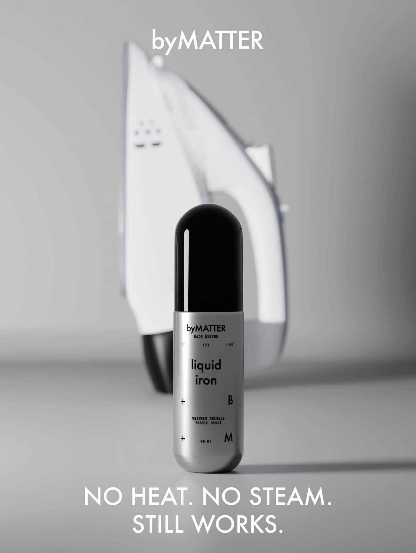 A byMATTER Liquid Iron bottle in sharp focus in the foreground, a traditional iron blurred and out of focus in the background — no heat, no steam, still works.