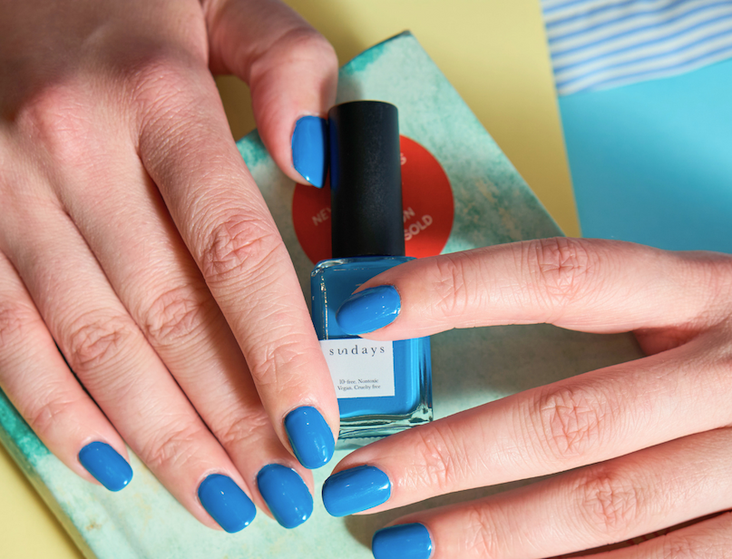 Close-up of a hand with bright ocean-blue nails resting on blue and yellow striped fabric.