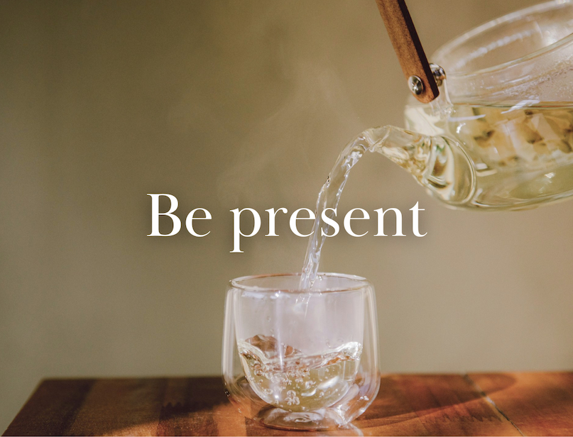 Tea being poured into a clear glass cup on a wooden table.