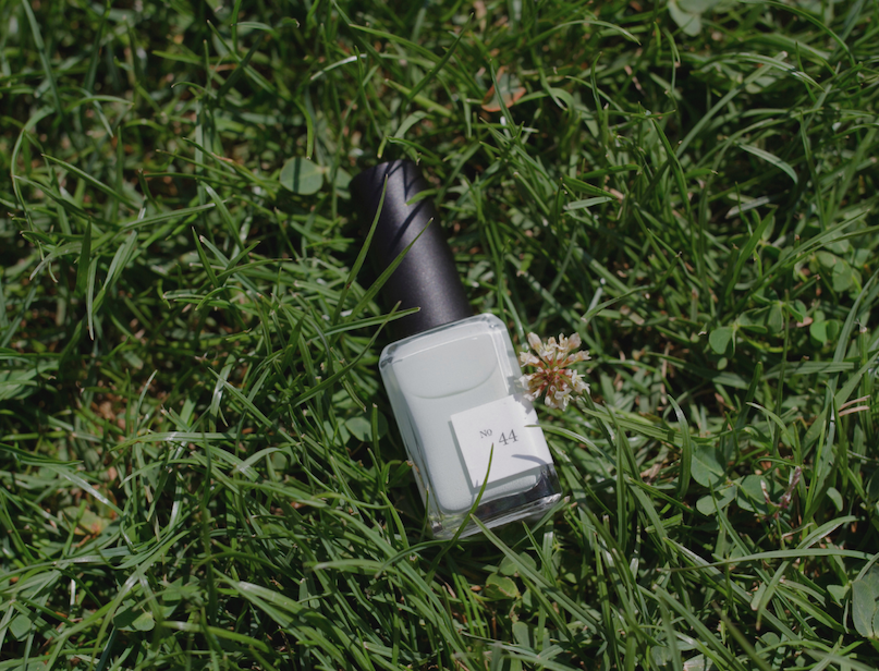 Bottle of pale mint-green nail polish resting in green grass outdoors.