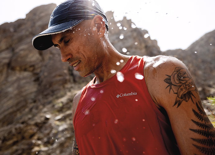 A man in a red shirt and black ball cap in a desert. 