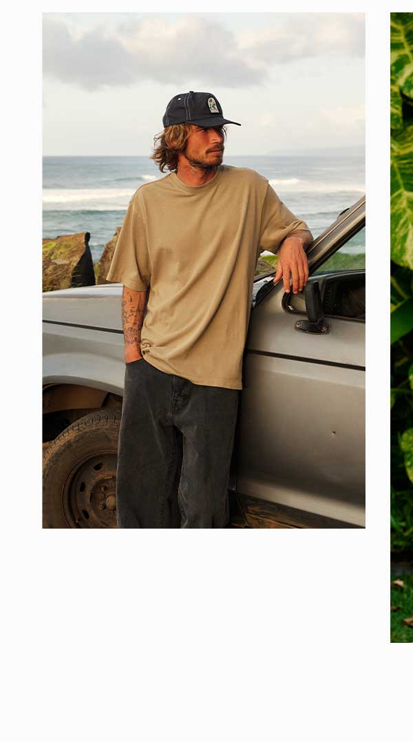 A Male model leaning against a trunk in the Box Fit Heritage Tee