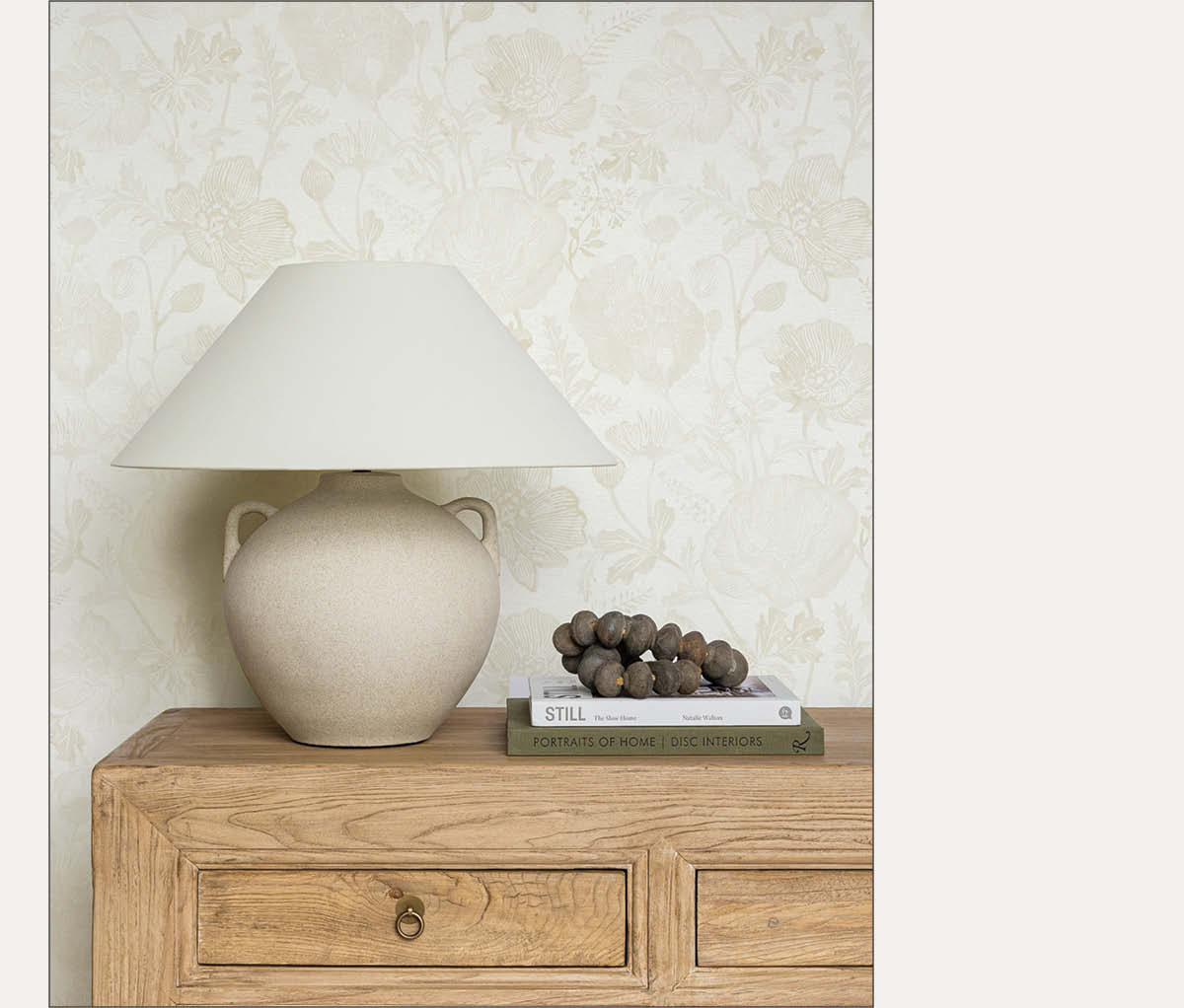 Image of Tempaper's Poppies wallpaper in Ivory by Pure Salt installed on a wall behind a light wood dresser with a beige lamp. 