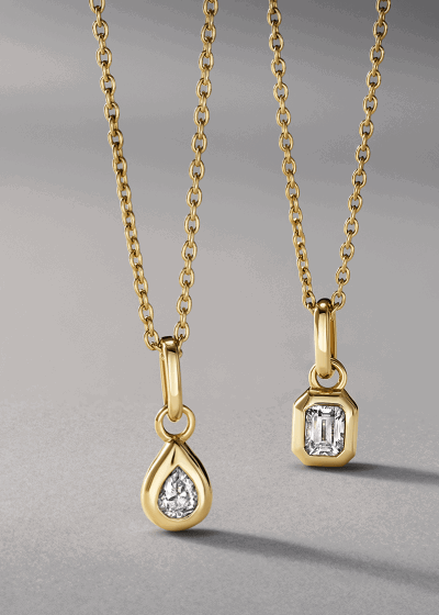 Two yellow gold bezel-set diamond pendant necklaces, one pear-shaped and one emerald-cut.