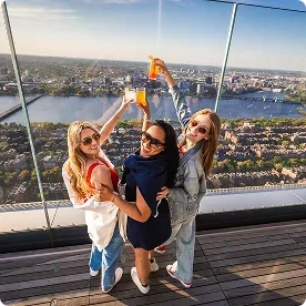 Three women toasting drinks at a rooftop bar.