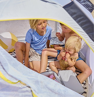 Children sitting in a beach tent with a cooler.