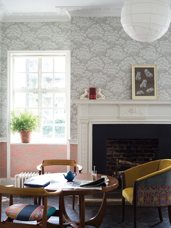 A traditional living room with an informal, relaxed feel. The walls are decorated with two colourways of Hornbeam wallpaper, with a wooden table in front and mid-century modern furniture. It has an eclectic, vibrant feel.