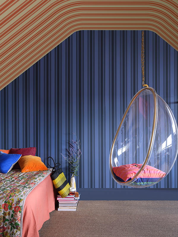 A playful bedroom layered with bold blue stripes, a striped sloping ceiling and a hanging bubble chair that adds movement and personality.