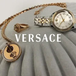 Collar de oro con un colgante circular, anillo de oro con una piedra y reloj de pulsera de metal bicolor exhibidos sobre una superficie gris con estrías.