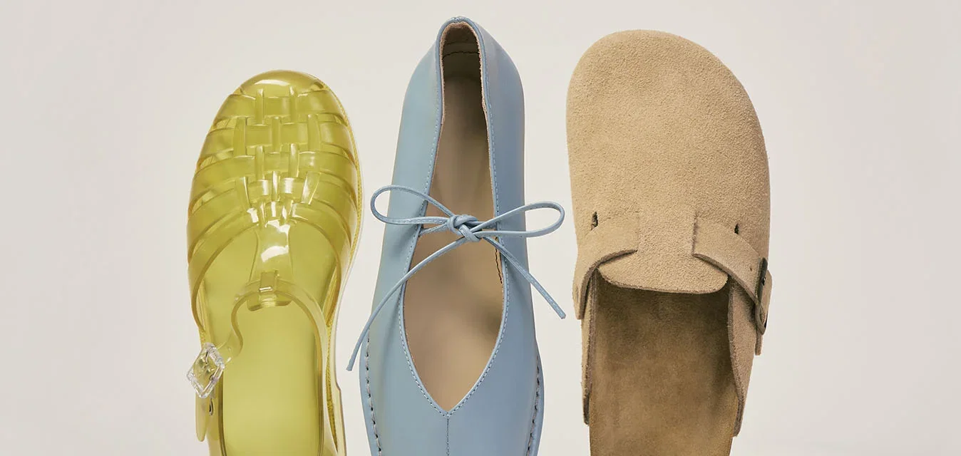 Una sandalia amarilla de gelatina, un zapato azul de cuero con cordones y un zapato marrón claro de ante sin cordones colocados uno al lado del otro sobre un fondo liso.