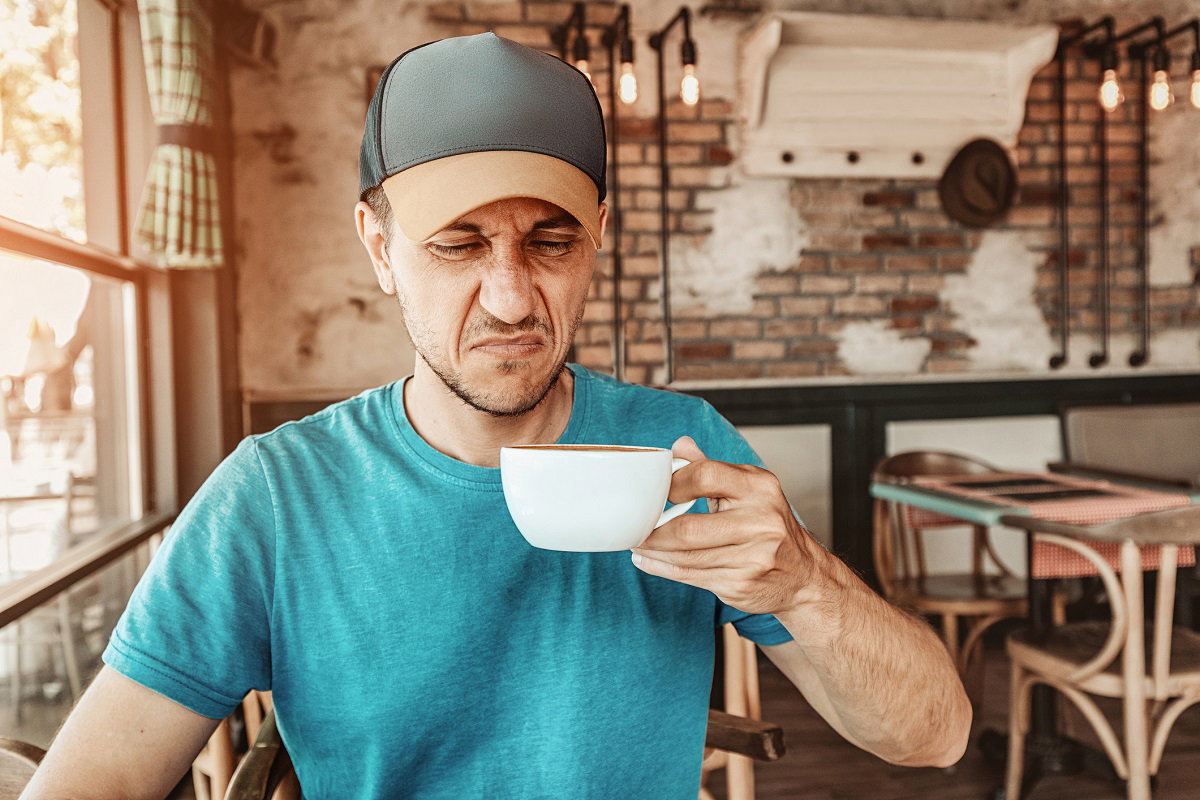 Un consommateur grimace en regardant sa tasse de café.