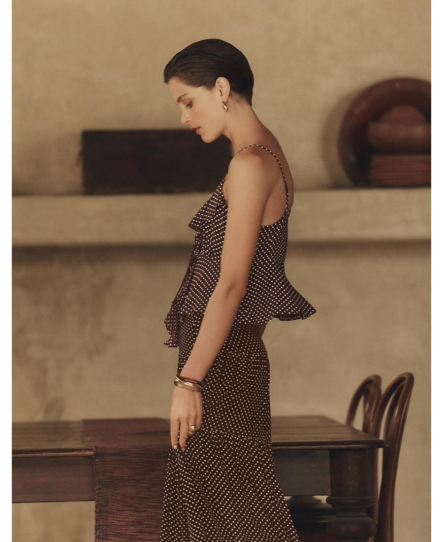 Woman wearing a matching polka dot print cami and skirt set in front of an outdoor dining table.