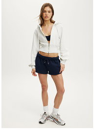 Woman wearing white cropped jacket and navy shorts with sneakers