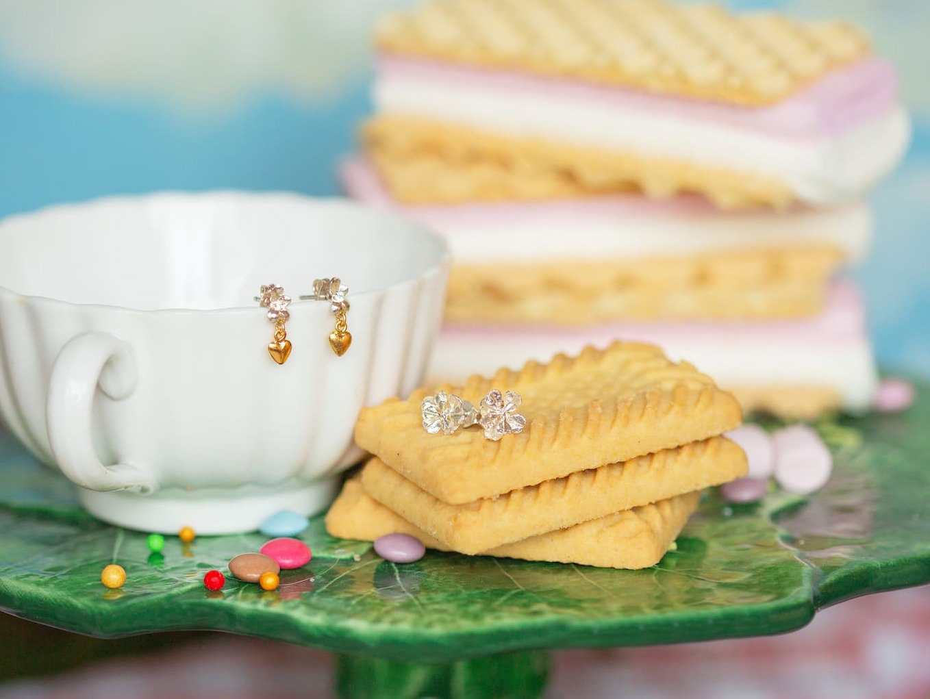 Alex Monroe Gold bee drop earrings and floral stud earrings styled with teacup, biscuits and pastel sweets.