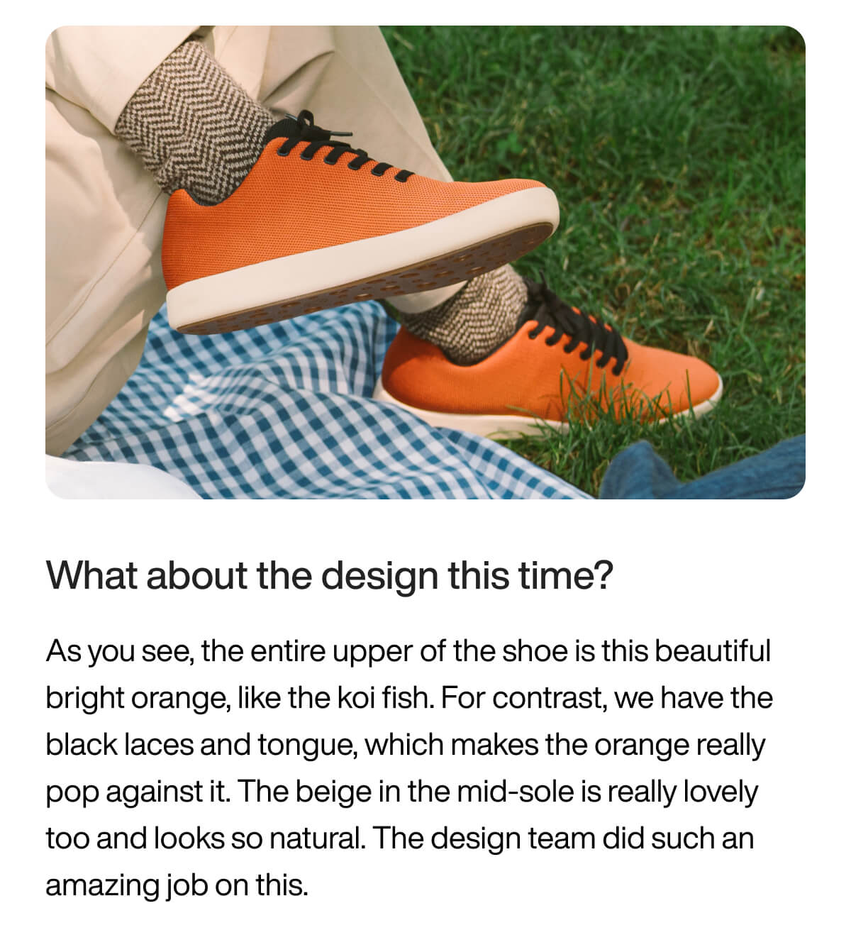 "Orange sneakers with black laces on grass, paired with beige pants and herringbone socks, next to a blue checkered blanket."