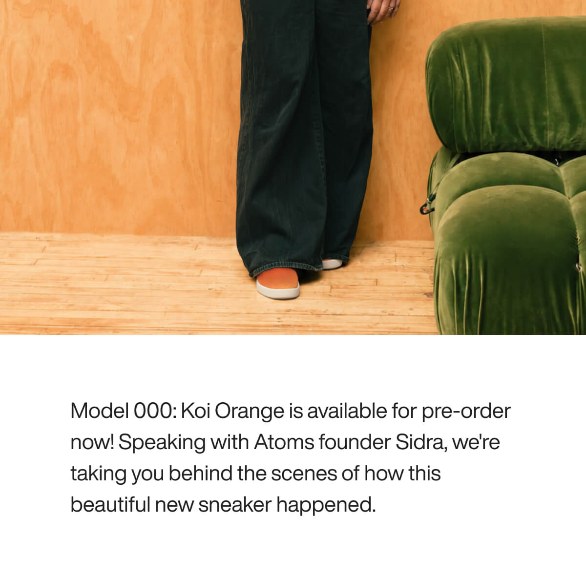 "Person wearing Koi Orange sneakers stands by a green couch on a wooden floor, highlighting the shoe's vibrant color."