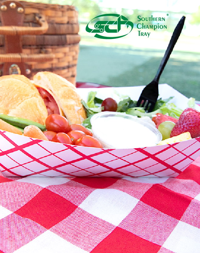 Southern Champion Tray paper food tray holding a sandwich, salad greens, cherry tomatoes, fruit, and dipping sauce on a red checkered picnic tablecloth.