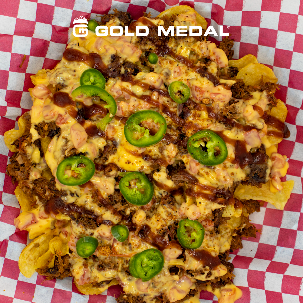 Gold Medal loaded nachos topped with melted cheese, chili, and sliced jalapeños, served in a red checkered food basket liner.