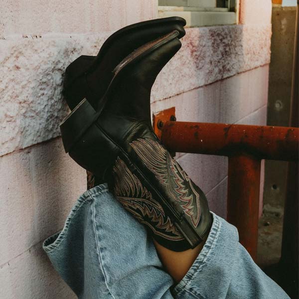 Person wearing Tony Lama boots leanig their feet against a wall cross legged.
