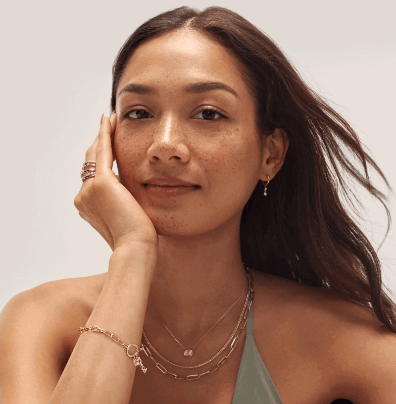 Woman wearing layered gold necklaces, a gold bracelet, stacked rings, and gold drop earrings.