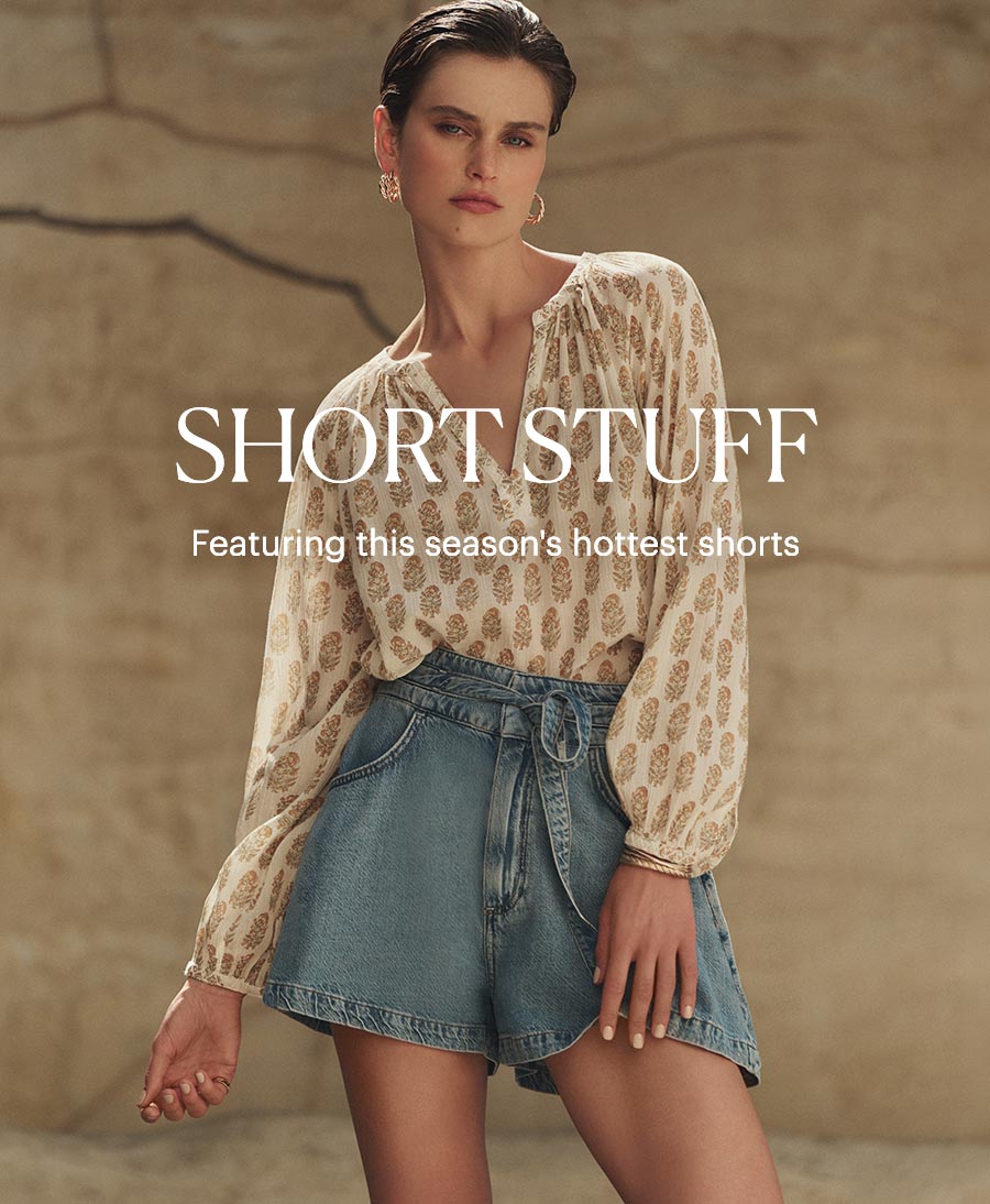 Short Stuff - Featuring this season's hottest shorts. Woman standing outdoors in a cream print blouse and tie-waist wide-leg denim shorts.