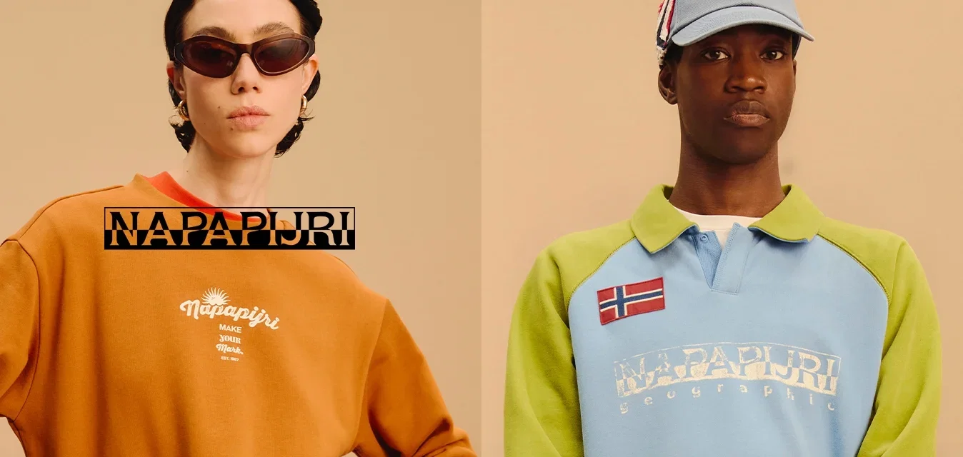 Due modelli indossano magliette del marchio Napapijri; uno con felpa arancione e occhiali da sole, l'altro con polo blu-verde e cappello.