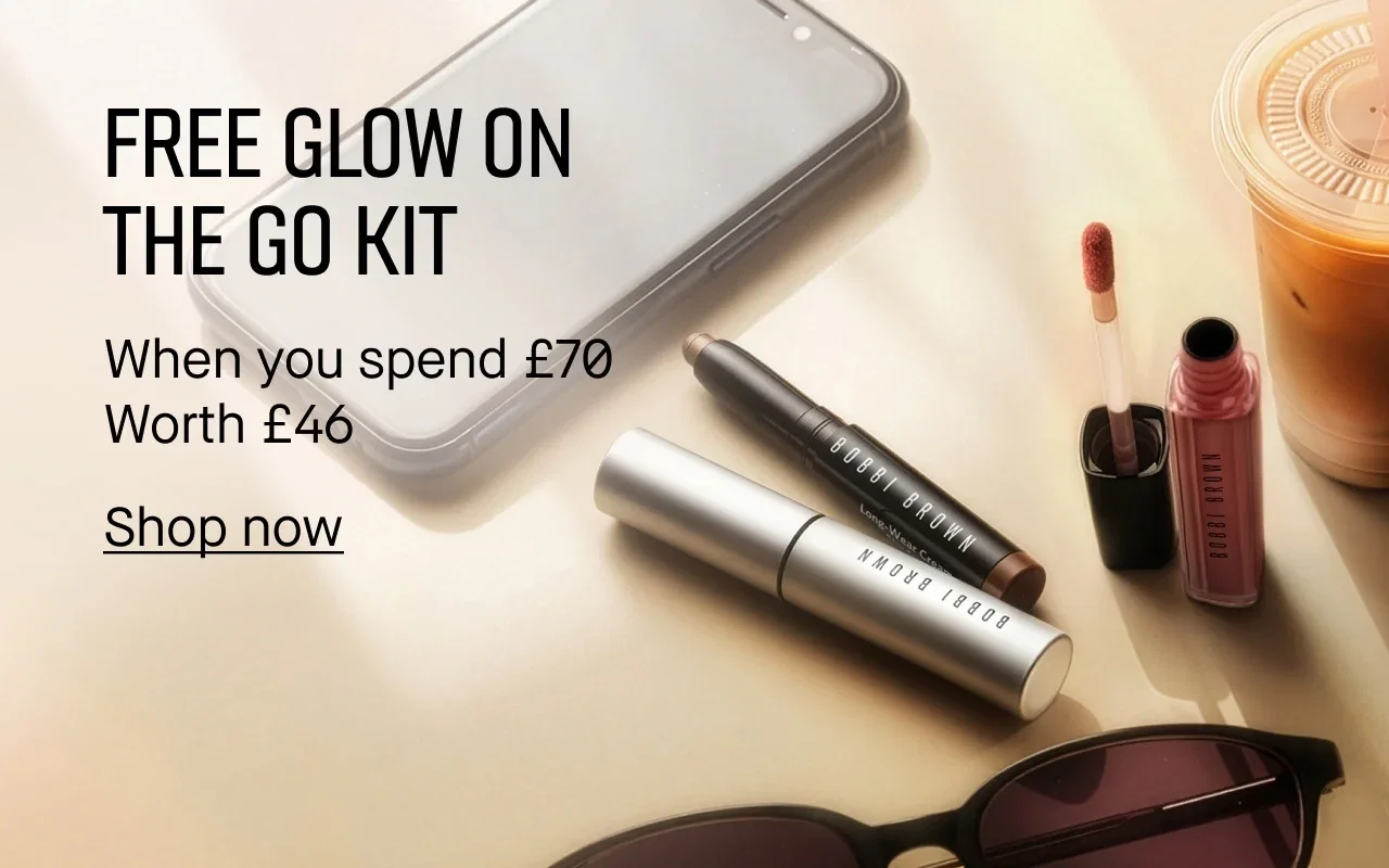 Flat lay of Bobbi Brown beauty products with a smartphone and an iced coffee drink on a light gradient background, with promo text reading, 'Free Glow On The Go Kit when you spend £70. Worth £46'.