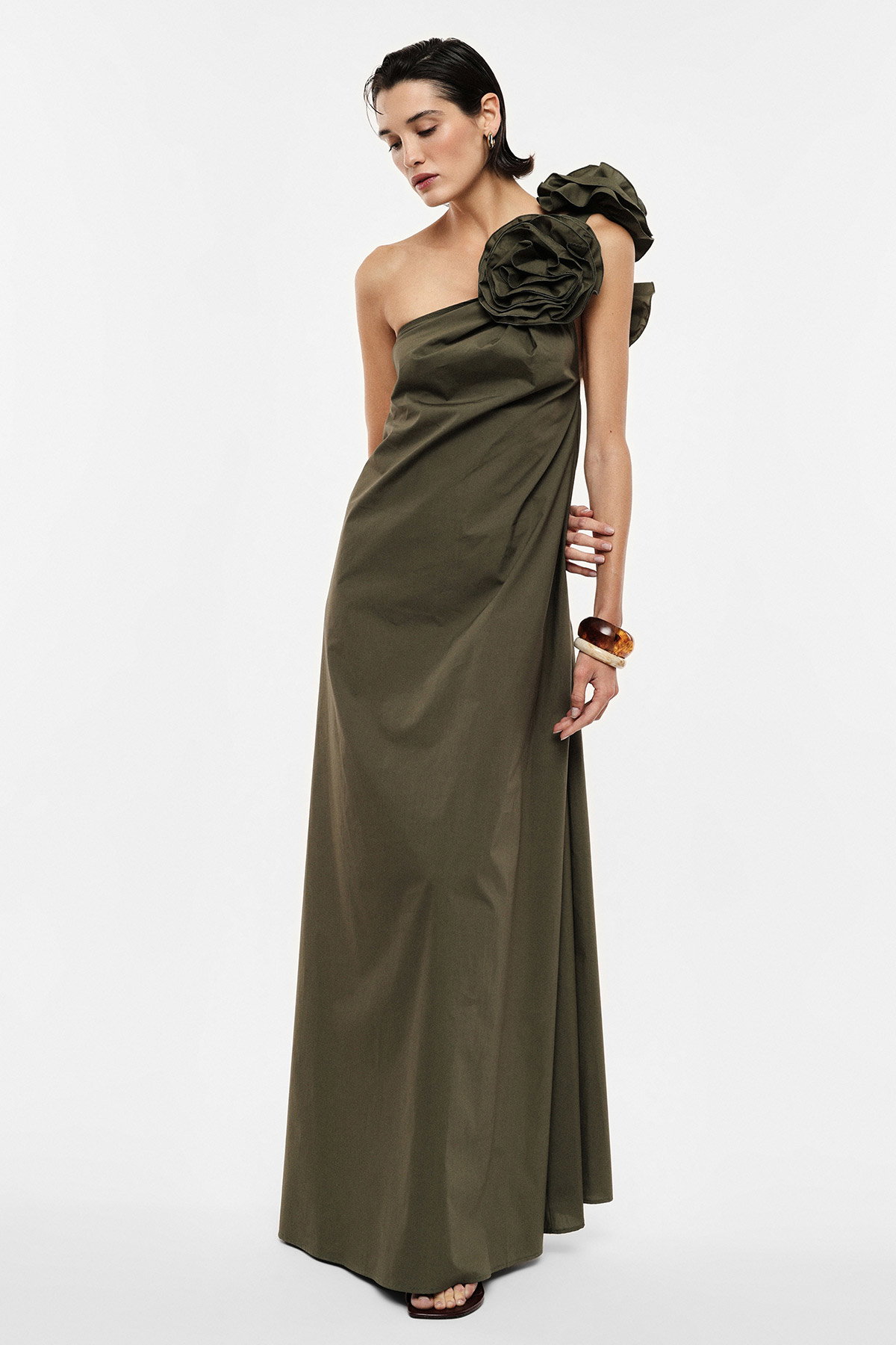 Model wearing olive one-shoulder evening gown with oversized floral shoulder detail, full-length elegant dress on plain white background