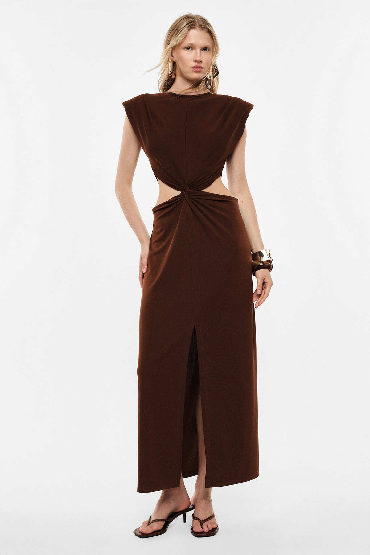 Woman modelling brown cut-out maxi dress with twisted knot and front slit, wearing sandals and bangles