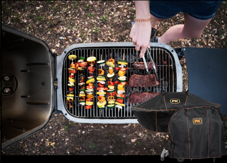 PK Grill cooking steaks and vegetable skewers outdoors with a Premium Grill Cover included in the promotion.