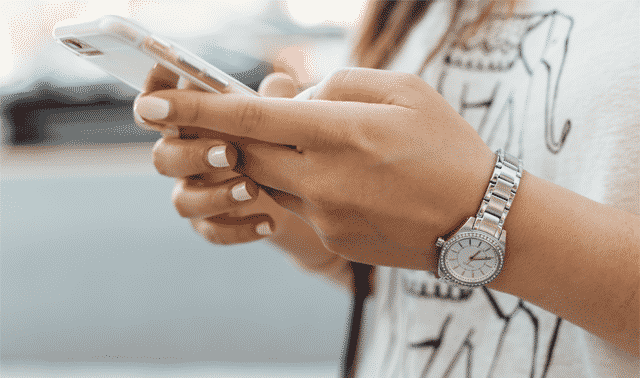 A person wearing a silver watch is holding and using a smartphone.