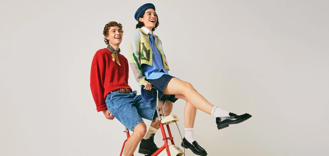Deux jeunes rient en étant assis sur un vélo d'exercice rouge dans une pièce simple aux couleurs claires.