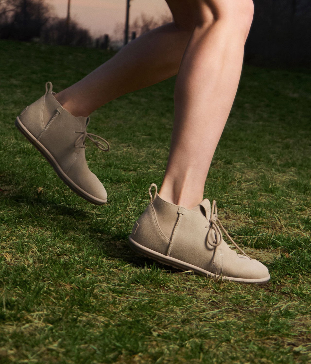 Close-up of a persons legs standing on grass, wearing UGGs from the Deconstructed collection.