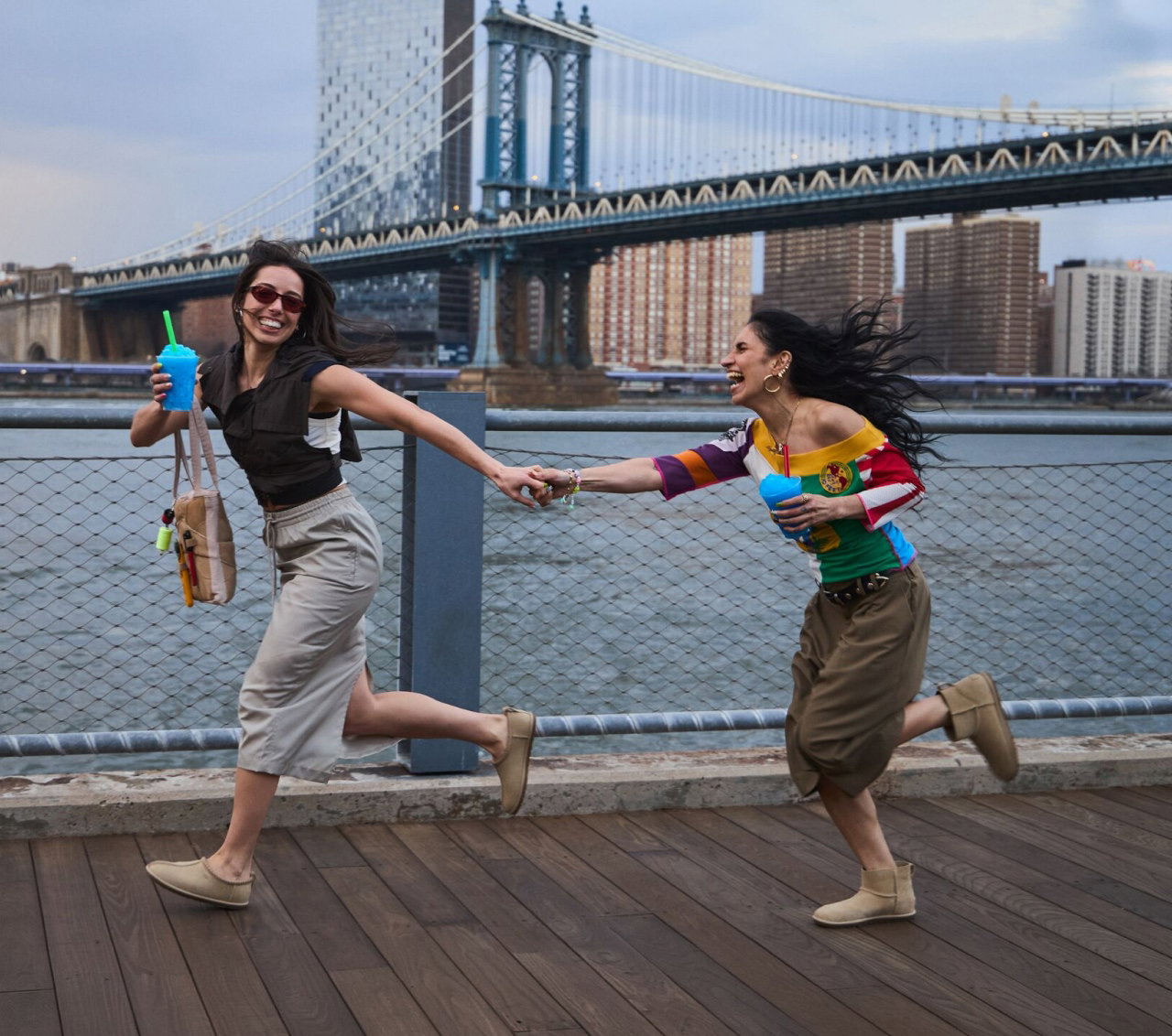 Two people running across a bridge holding hands, wearing UGGs from the Deconstructed collection.