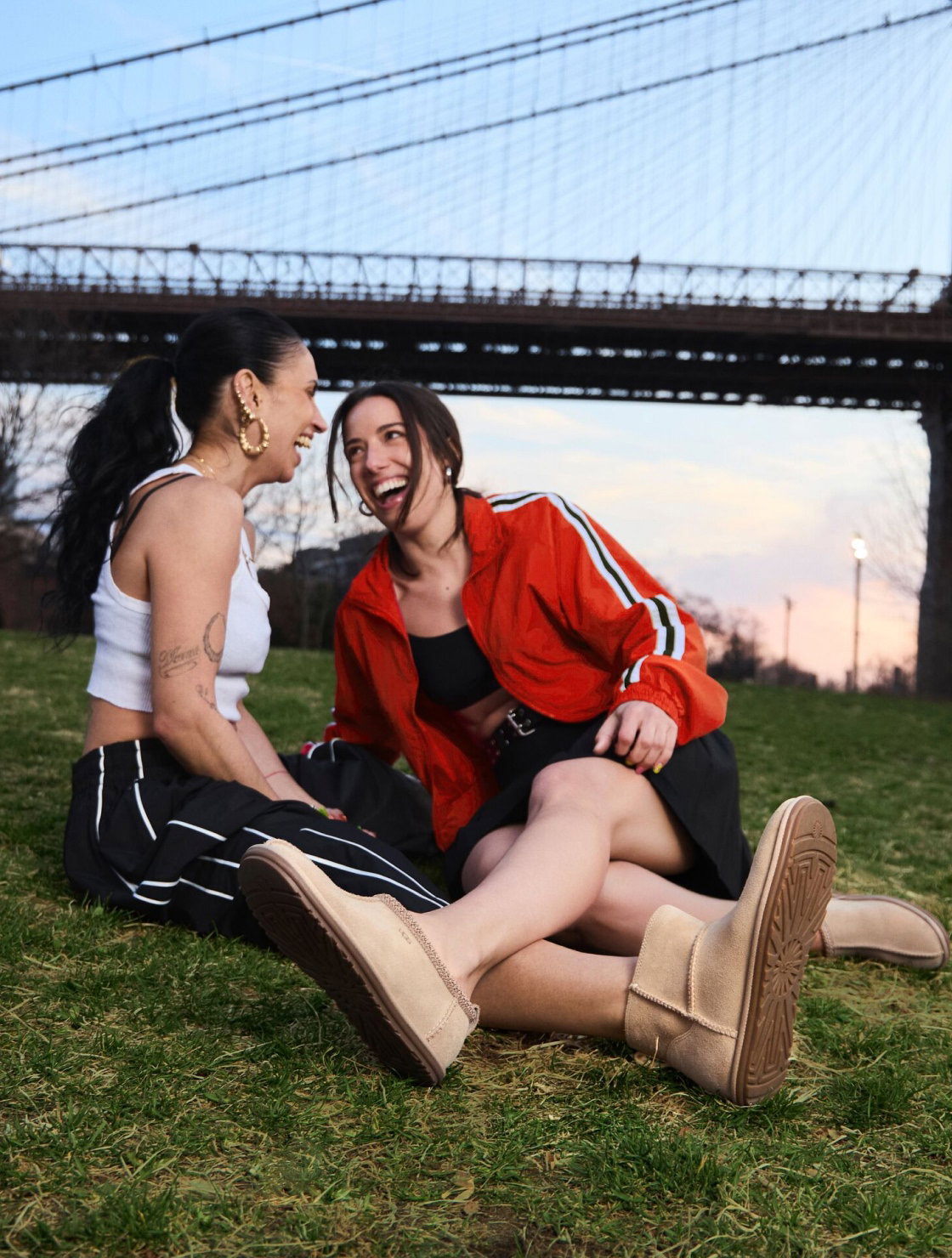 Two people sat on grass by a bridge, wearing UGGs from the Deconstructed collection.