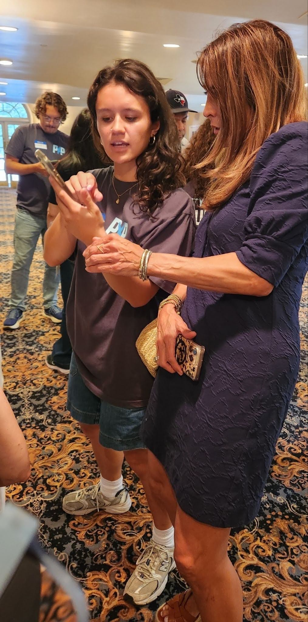 A PxP volunteer showing her phone to a woman in a blue dress on the right of the image