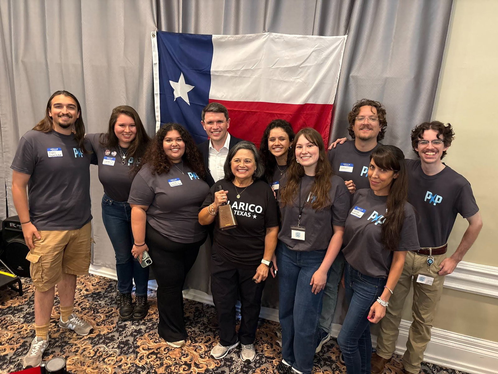 Group of Powered by People volunteers wearing gray tee shirts standing in two rows, with James Talarico standing in the middle of the back row. The group is standing in front of the Texas flag