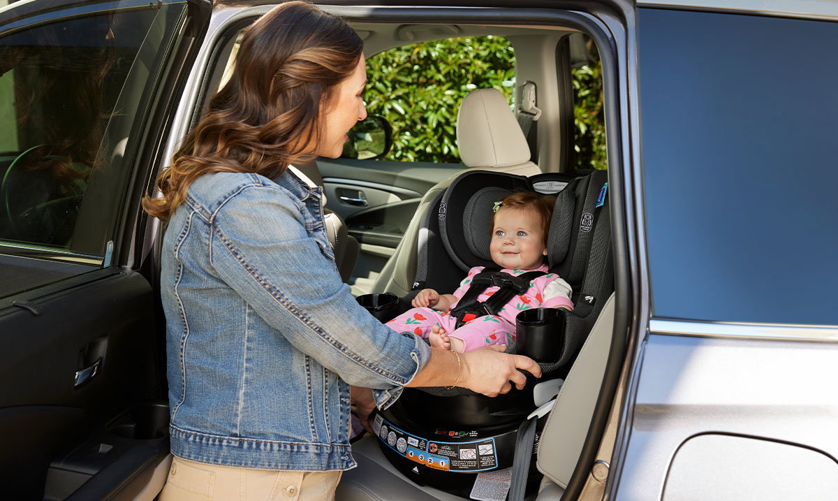 Mom smiling at baby buckled into a Graco car seat in the back seat of a car.