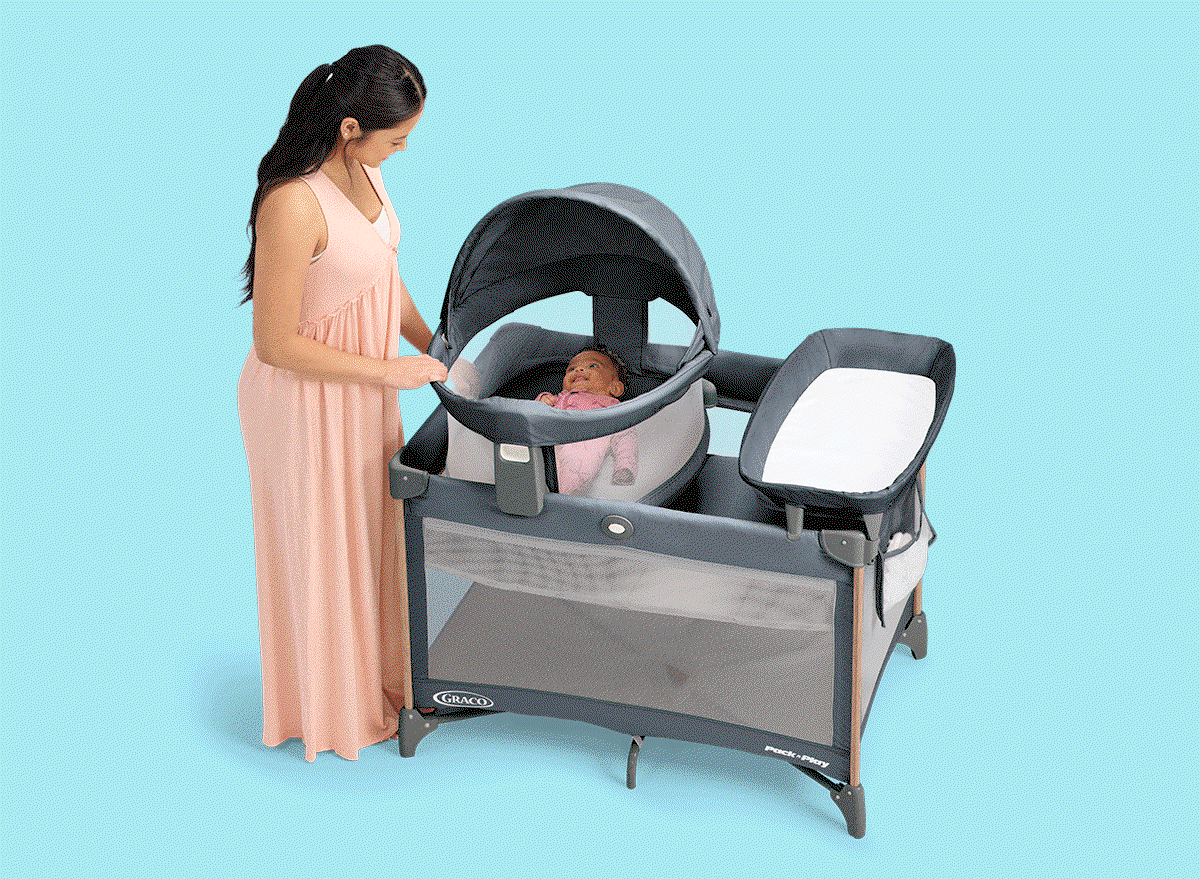Mom placing smiling baby into a Graco Pack 'n Play playard with bassinet and changing station.