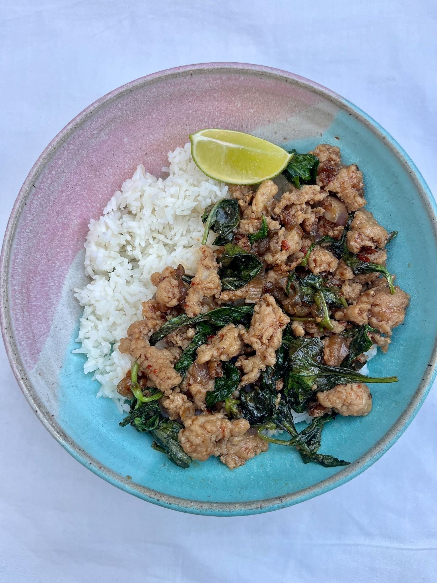 Basil and ground chicken on white rice in a white bowl