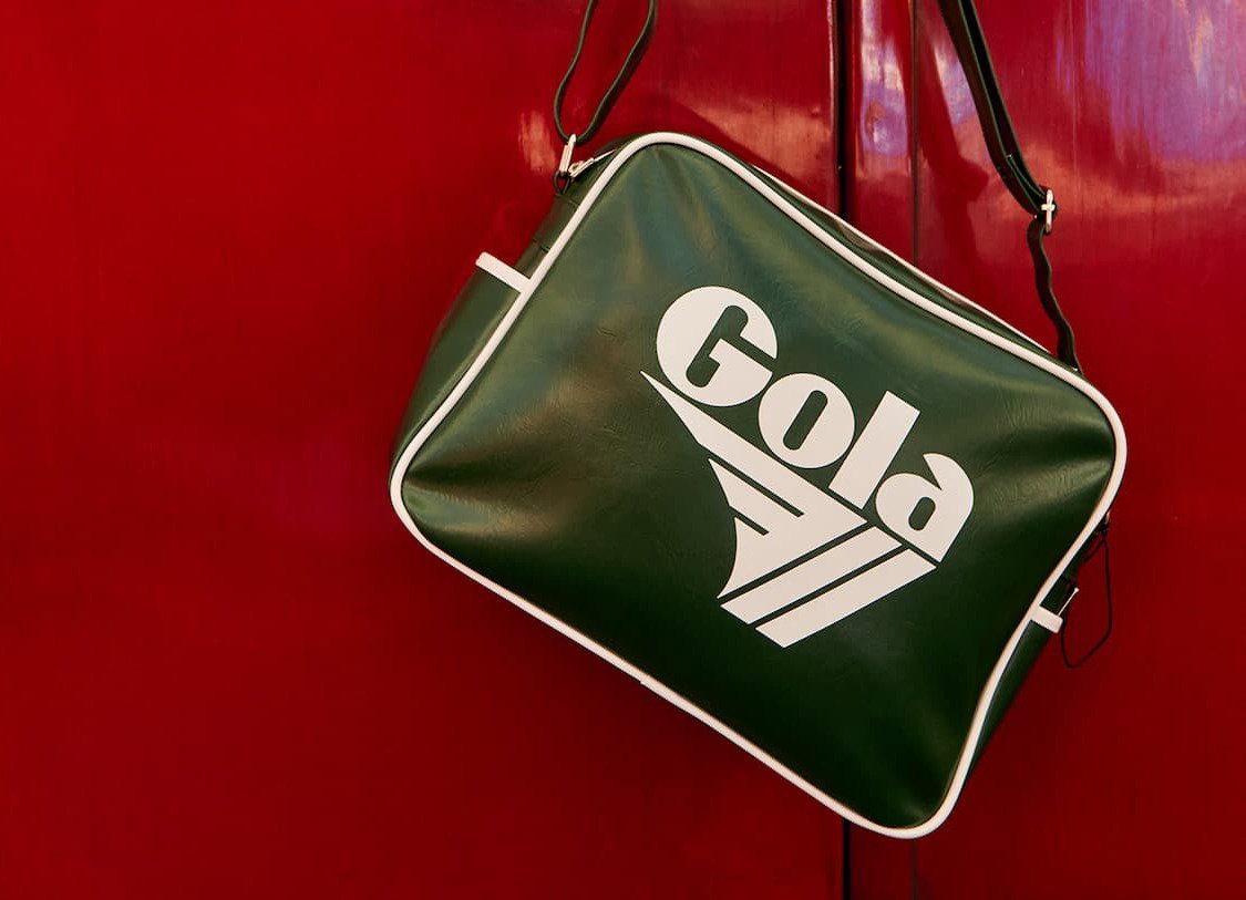 An image of a Gola Redford bag hanging on a red door. 