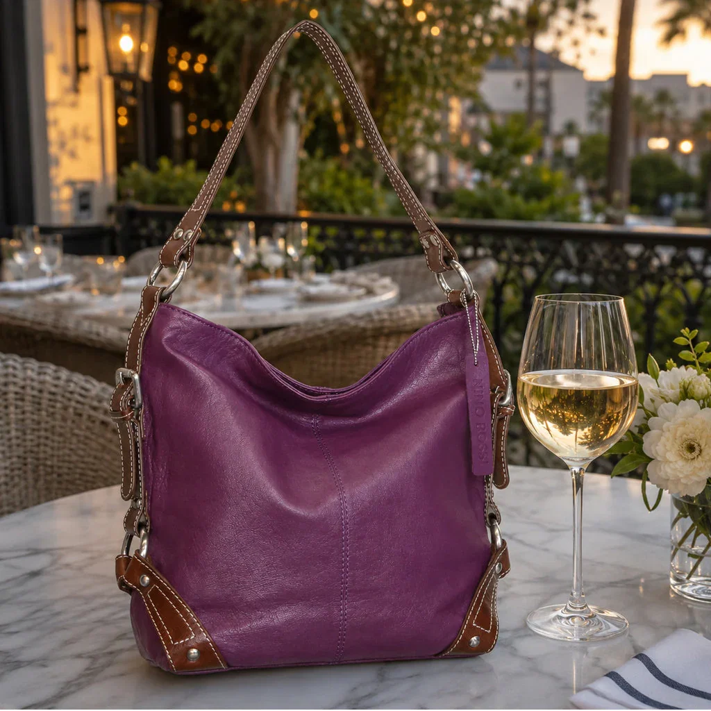 Purple leather hobo bag displayed on marble table with wine glass and flowers at elegant rooftop dining setting.