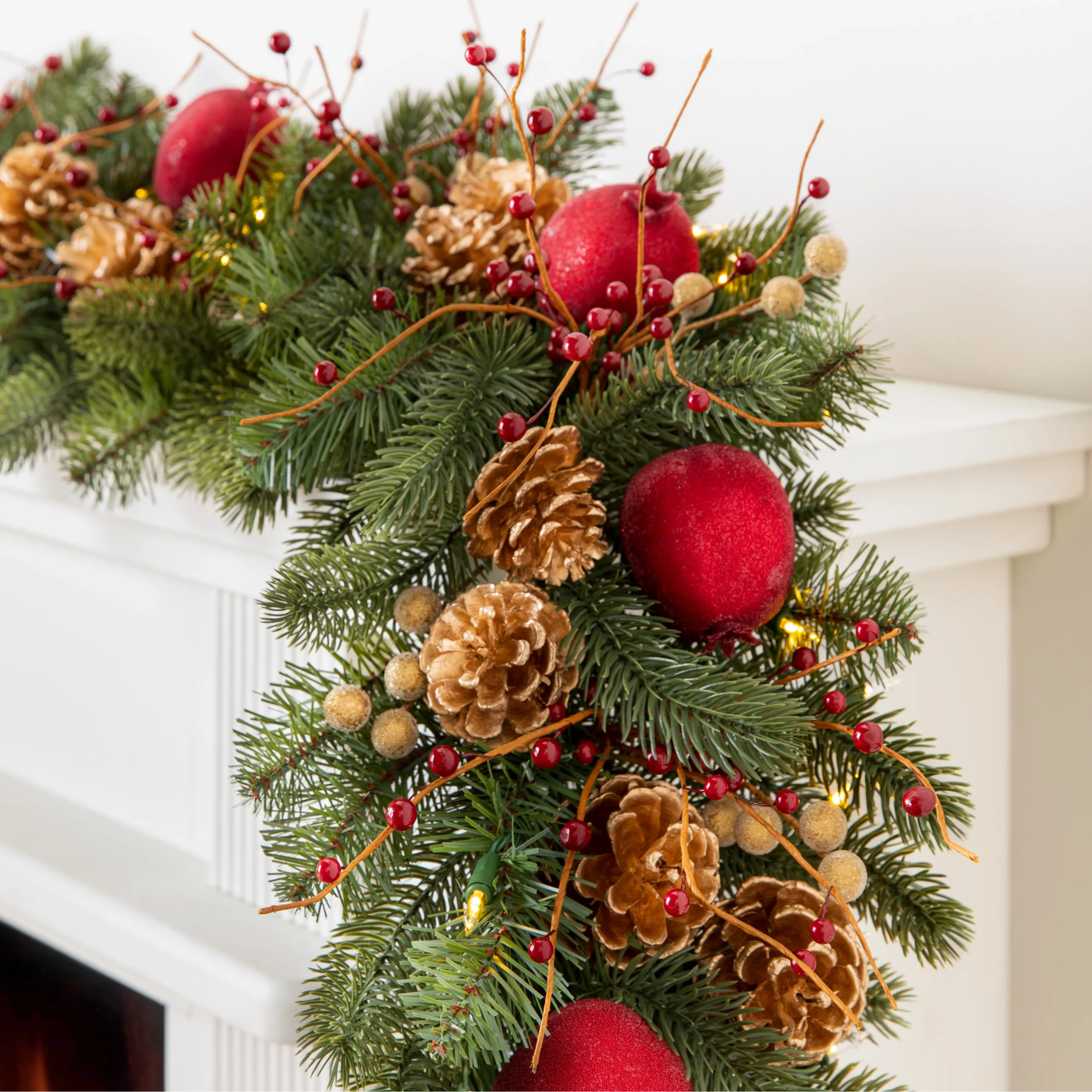 Pre-lit Christmas garland with red ornaments, gold pinecones, berries, and greenery draped over a white mantel.