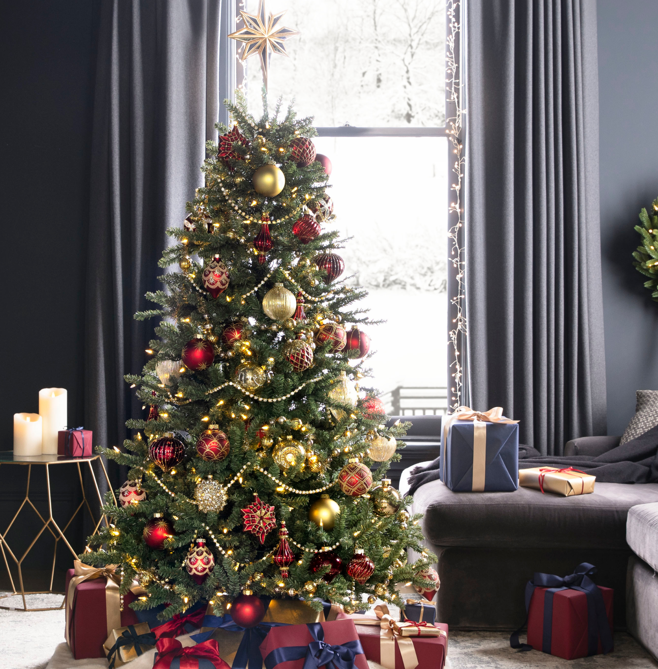 Pre-lit Christmas tree decorated with red and gold ornaments, topped with a star and surrounded by wrapped gifts in a cozy living room.