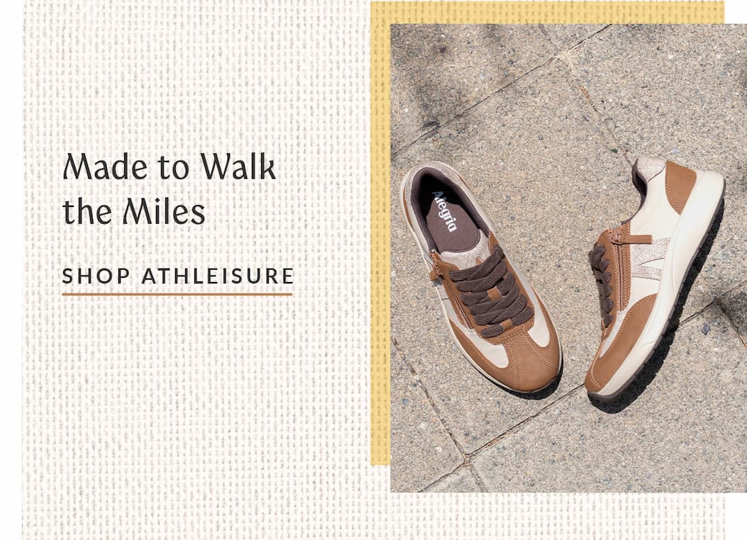A top-down view of a pair of brown and beige athletic sneakers with side zippers resting on a grey concrete pavement. On the left side, text on a light textured background reads "Made to Walk the Miles" above an underlined "SHOP ATHLEISURE" link.