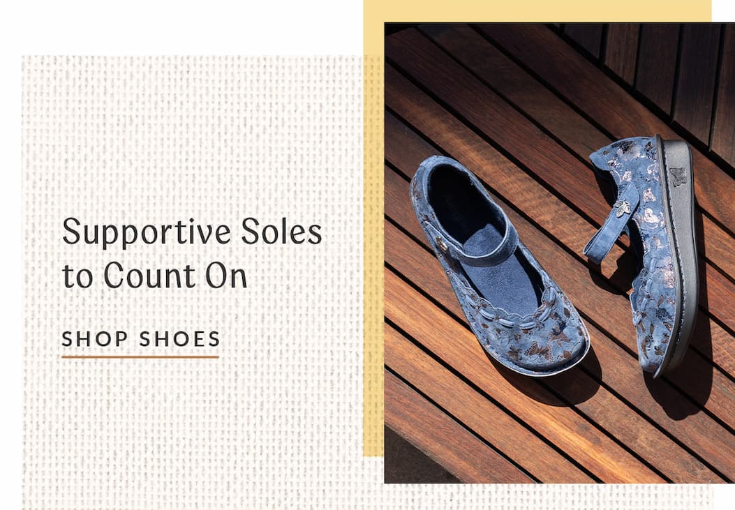 A pair of blue textured suede Mary Jane shoes with a subtle butterfly and floral pattern are displayed on a dark wooden slatted surface under bright sunlight. On the left, text on a light textured background reads "Supportive Soles to Count On" above a underlined "SHOP SHOES" link.